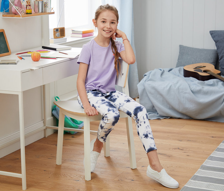 Dziewczyna siedzi na krześle przy biurku, ubrana w stretchowe spodnie dżinsowe.