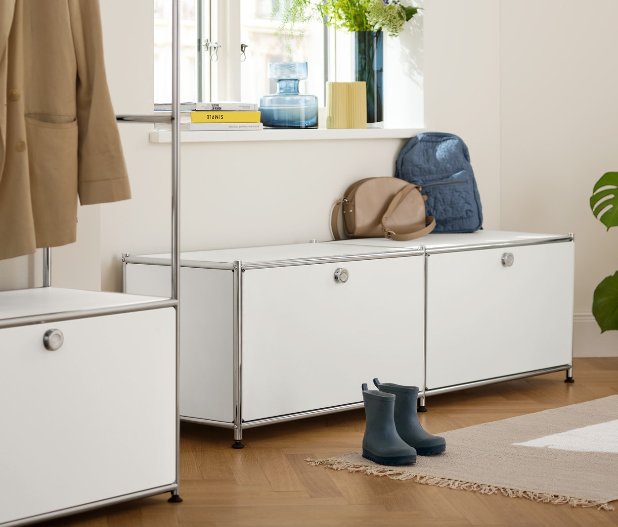 Wnętrze z metalową garderobą „CN3” z drążkiem na ubrania i niską szafką metalową »CN3« z szufladami, białą. Na szafce leżą torba i plecak.