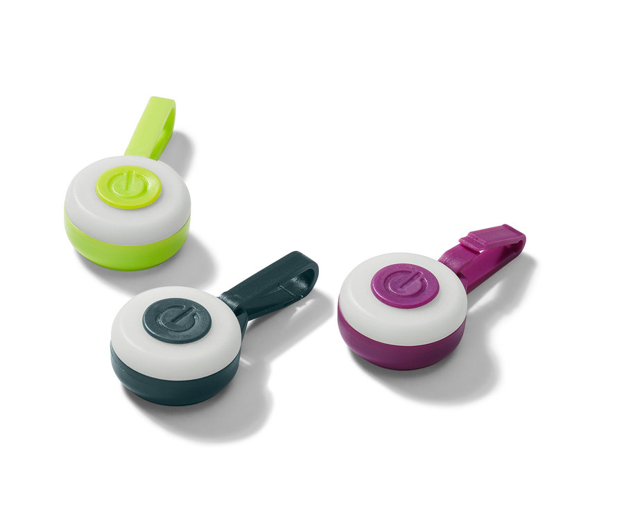 Trzy przywieszki LED w kolorach zielonym, granatowym i fioletowym leżą na białej powierzchni.