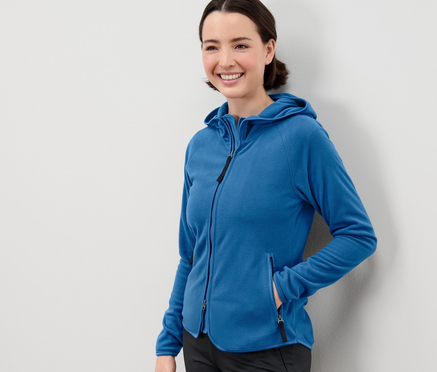 Kobieta pozuje w niebieskiej bluzie polarowej z kapturem.