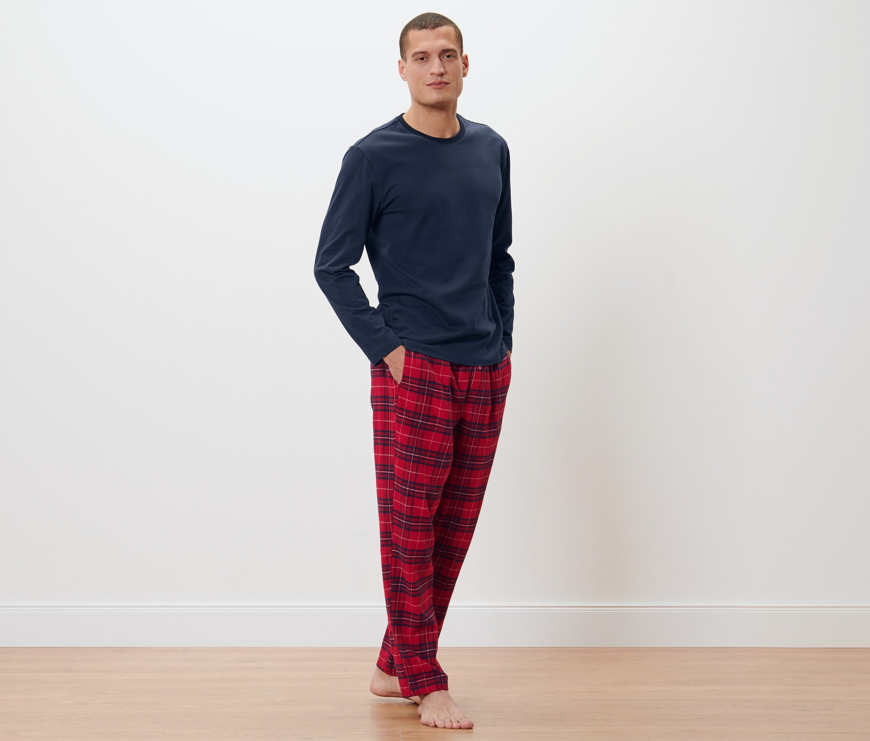 Mężczyzna pozuje w granatowej piżamie i spodniach flanelowych w kratę.