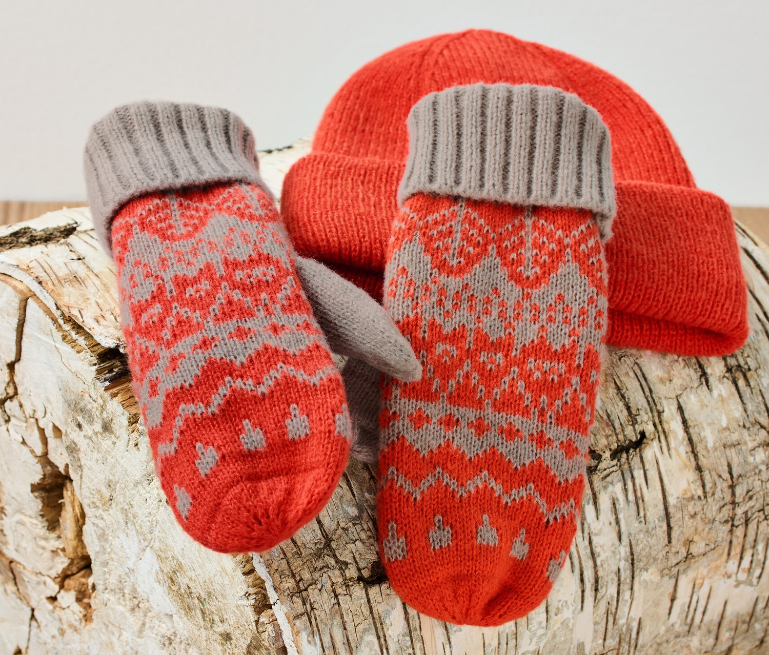 Dzianinowe rękawiczki z jednym palcem i pomarańczowa czapka leżą na kłodzie brzozy.