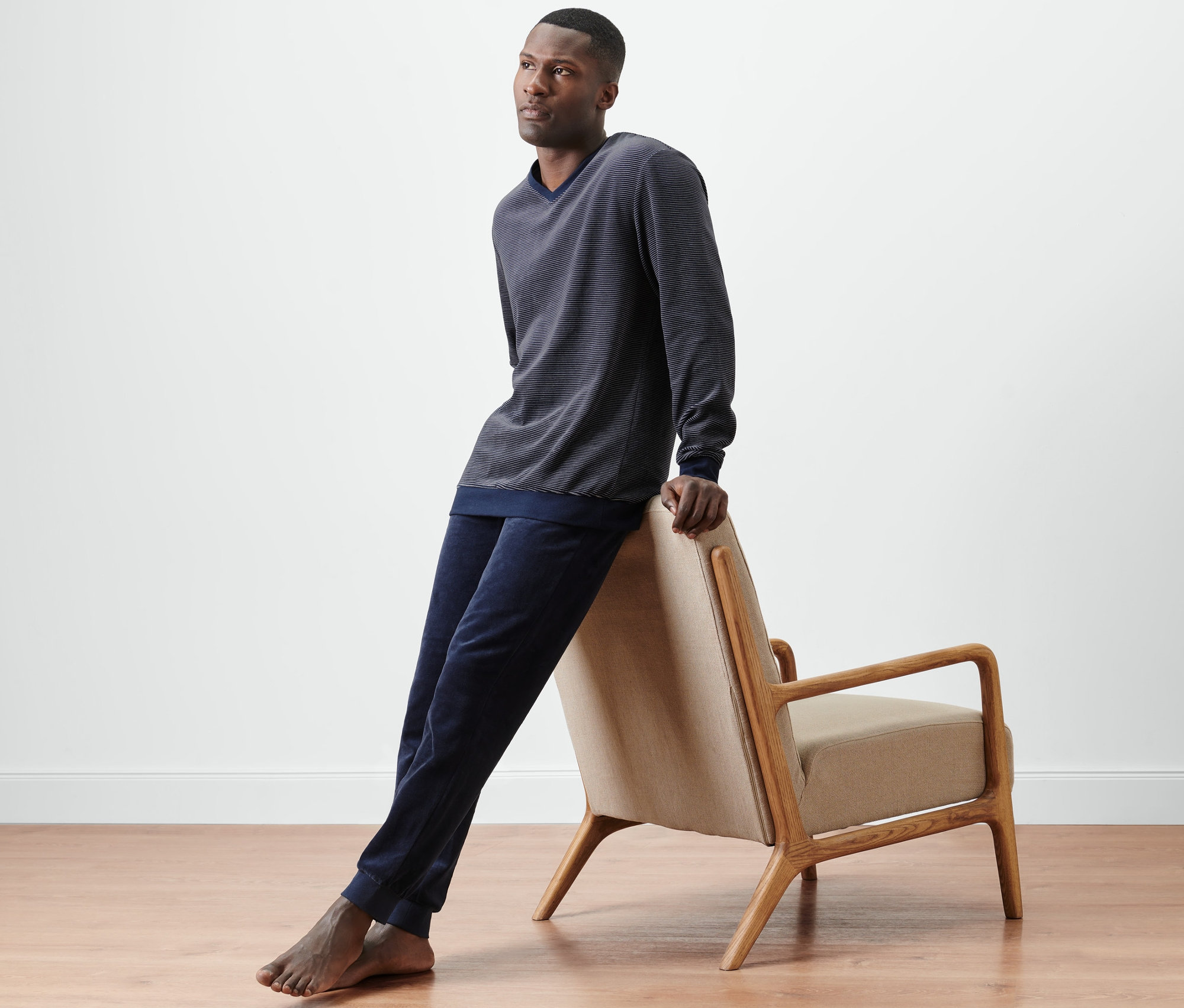 Mężczyzna opiera się o krzesło, ubrany w granatowo-szarą piżamę z weluru.