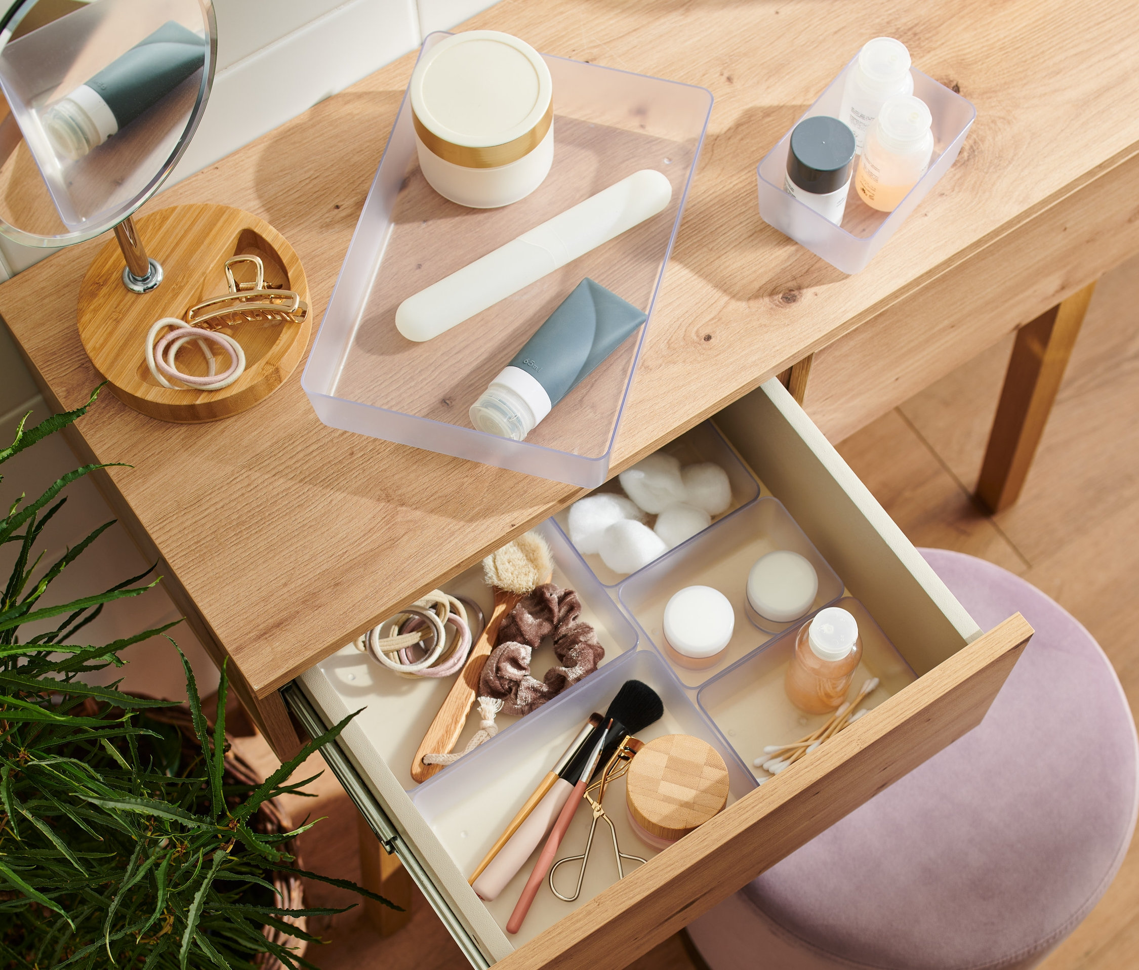 Otwarta szuflada drewnianej toaletki zawiera zestaw organizerów do szuflad z kosmetykami.