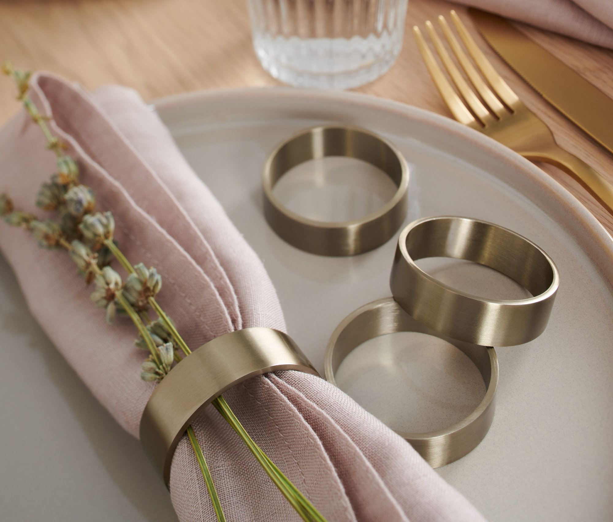 Na talerzu leży różowa serwetka z dekoracją i pierścieniami na serwetki stołowe, 4 sztuki. Obok leżą trzy pierścienie na serwetki.