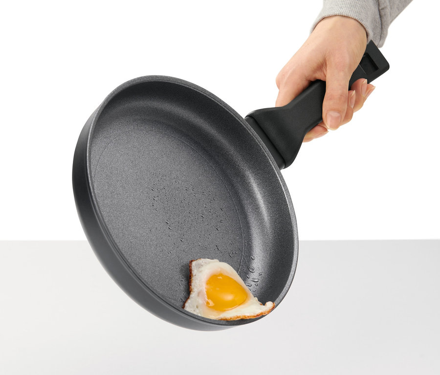 Ręka trzyma profesjonalną patelnię aluminiową z jajkiem sadzonym.