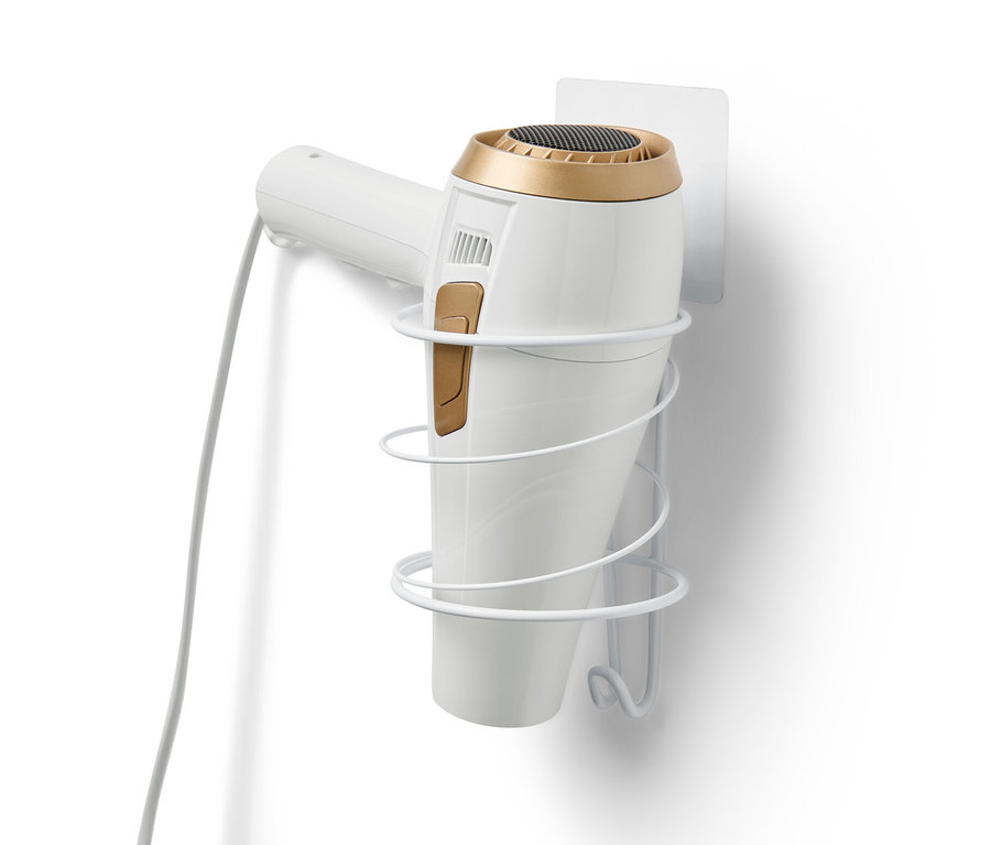 Biały uchwyt na suszarkę przymocowany jest do białej ściany i trzyma białą suszarkę do włosów.