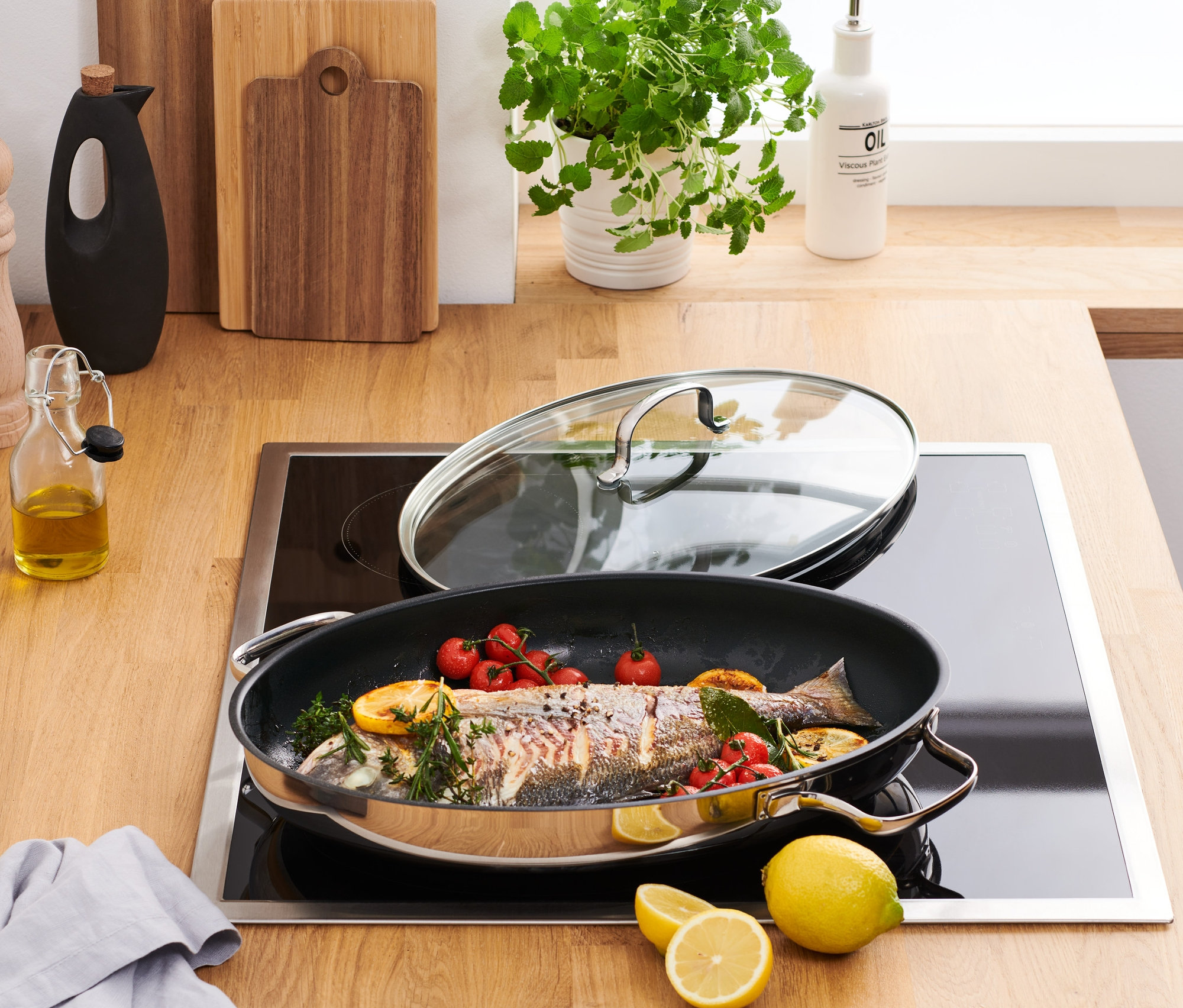 Na płycie indukcyjnej stoi patelnia ze stali szlachetnej do podawania potraw z rybą, pomidorkami cherry i cytryną.