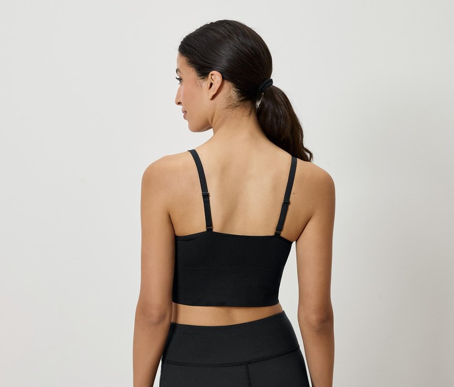 Widok z tyłu na kobietę z brązowymi włosami związanymi w kucyk, ubraną w czarny top sportowy i legginsy.