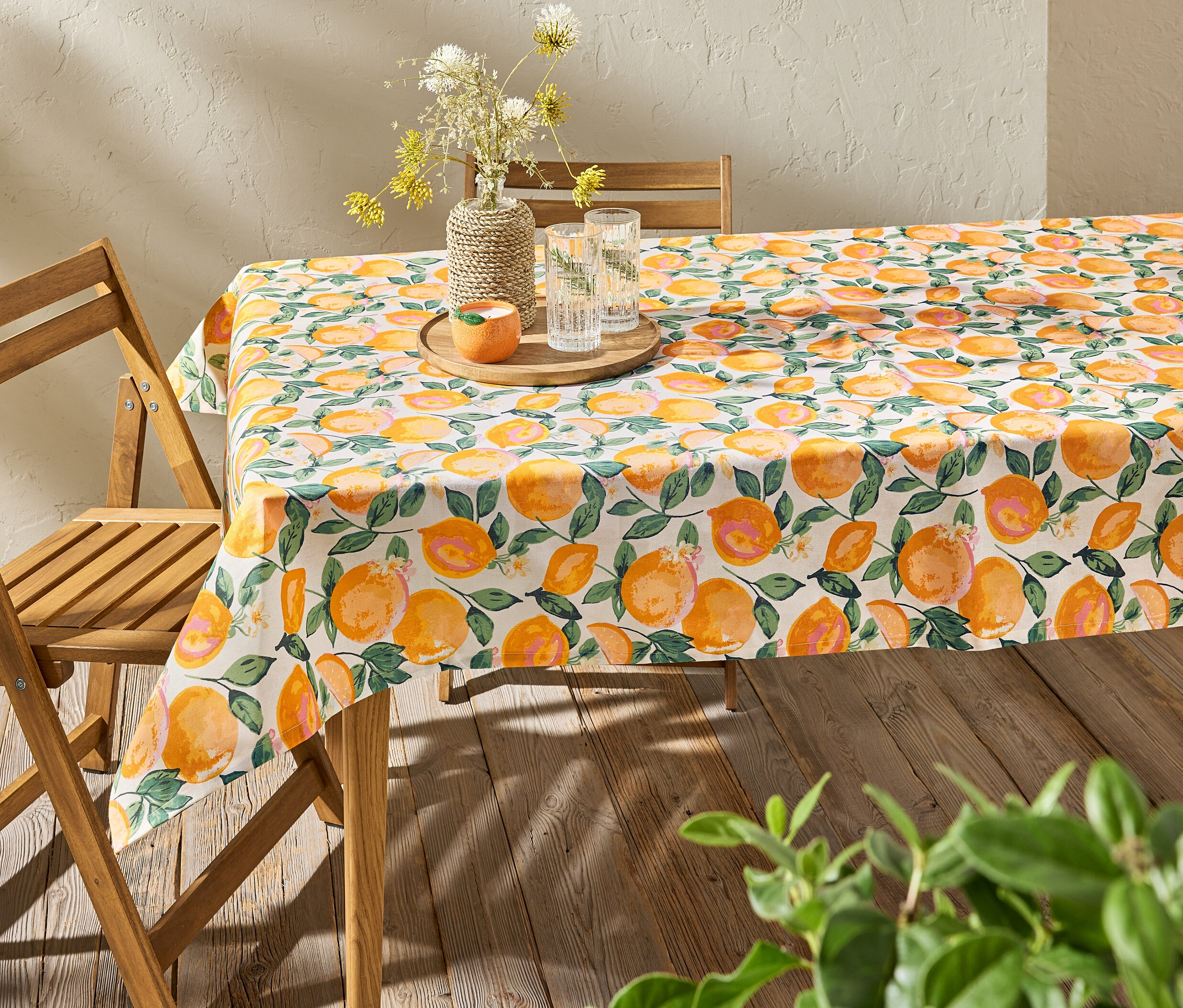 Stół z obrusem ogrodowym w cytrusy, na nim wazon z kwiatami i szklanki z wodą.