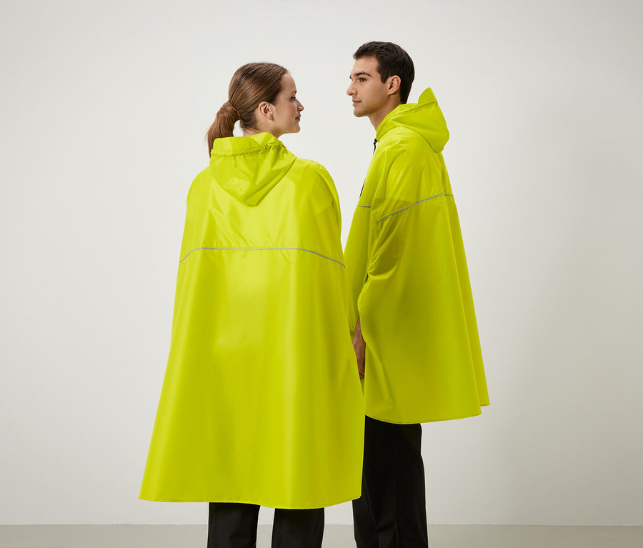 Dwie osoby stoją obok siebie, ubrane w żółte poncza przeciwdeszczowe z kapturem.