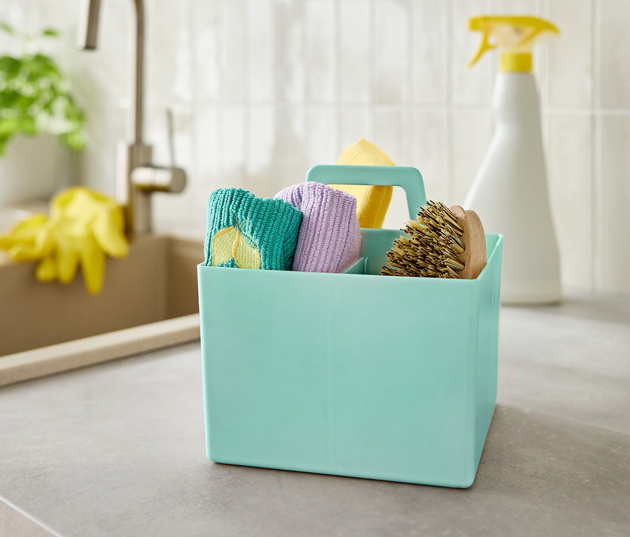 Turkusowe pudełko ze środkami czystości stoi na szarym blacie obok zlewu.