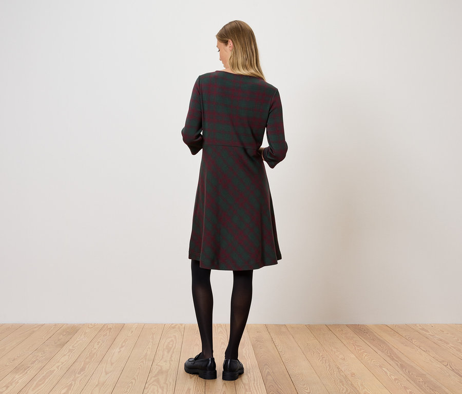 Kobieta stoi tyłem, ubrana w sukienkę w paski, czarne rajstopy i czarne buty.