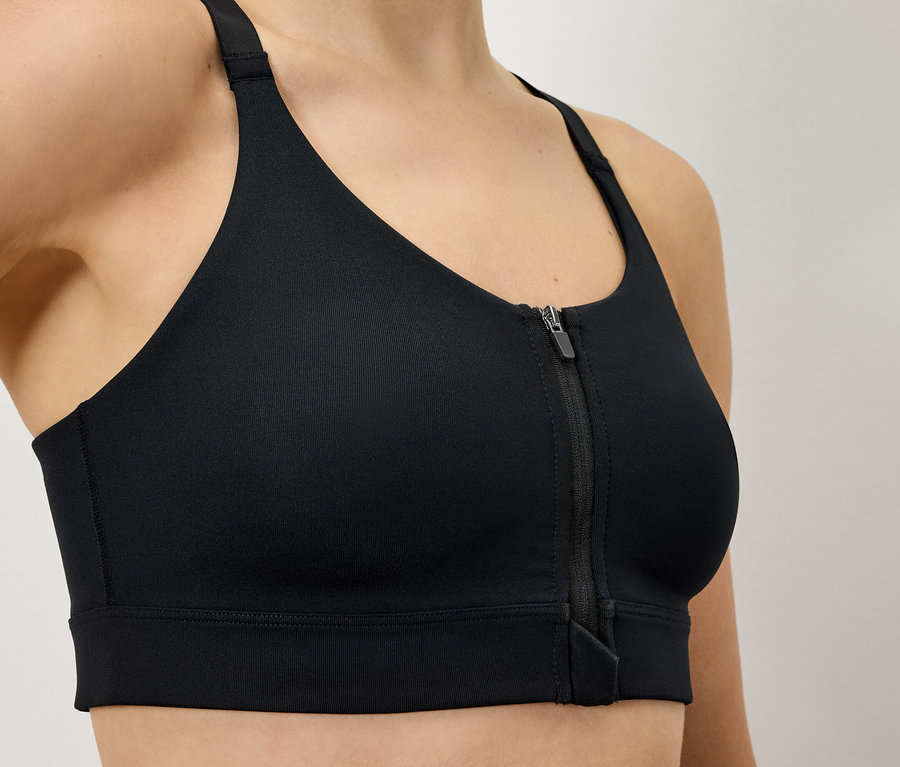 Kobieta ma na sobie czarny biustonosz sportowy zapinany na zamek błyskawiczny z przodu.