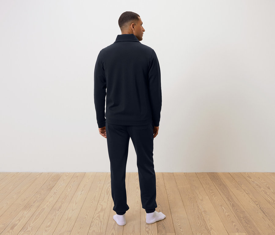 Mężczyzna tyłem do kamery w granatowej piżamie i białych skarpetach.