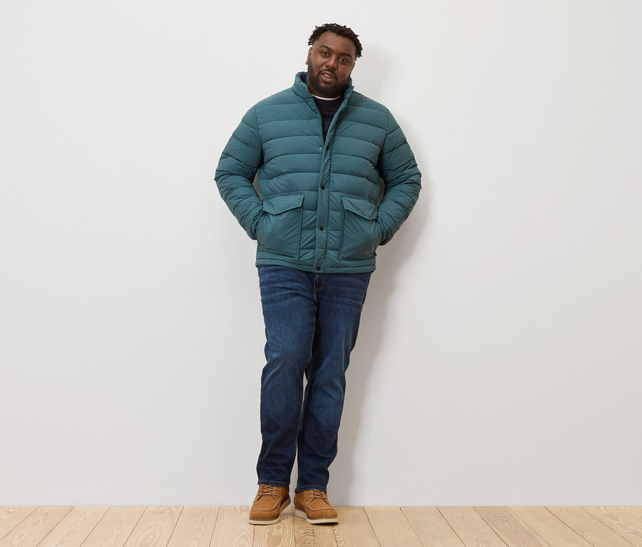 Mężczyzna stoi w pikowanej kurtce, dżinsach i butach.