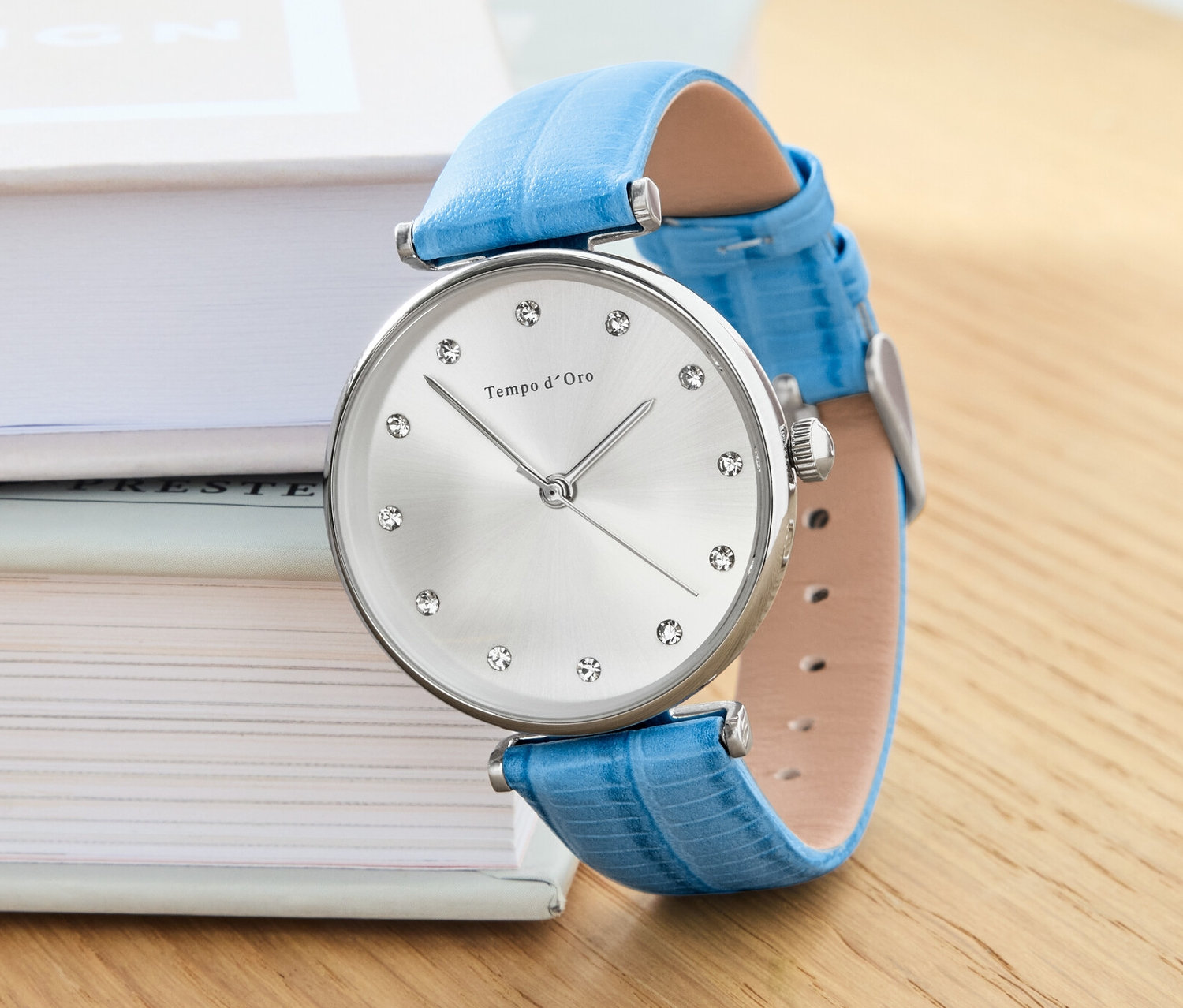 Zegarek ze skórzanym paskiem i kryształkami leży na książkach.