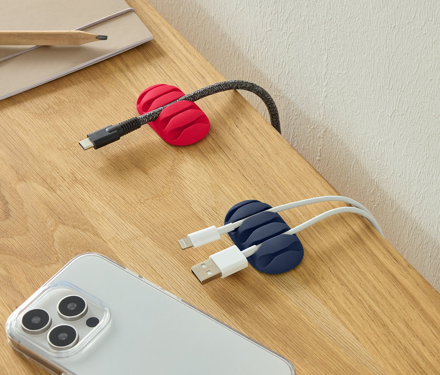 Kabel USB-C w czerwonym uchwycie na kable, dwa kable USB w niebieskim uchwycie na kable i smartfon na biurku.