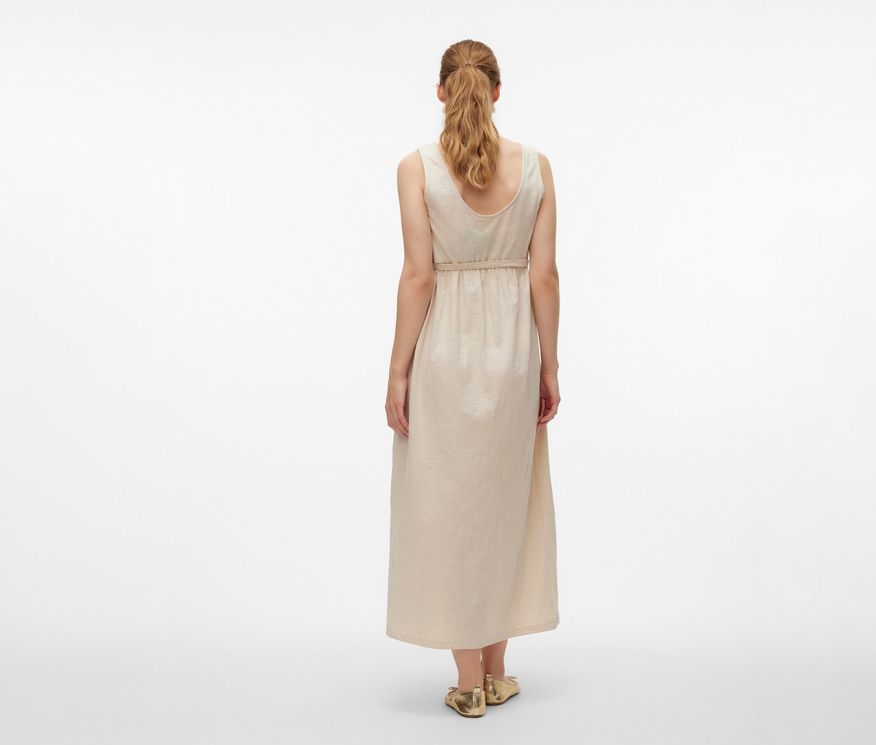 Widok z tyłu kobiety w sukience ciążowej MAMALICIOUS „MLEVI LIA” i złotych butach na białym tle.