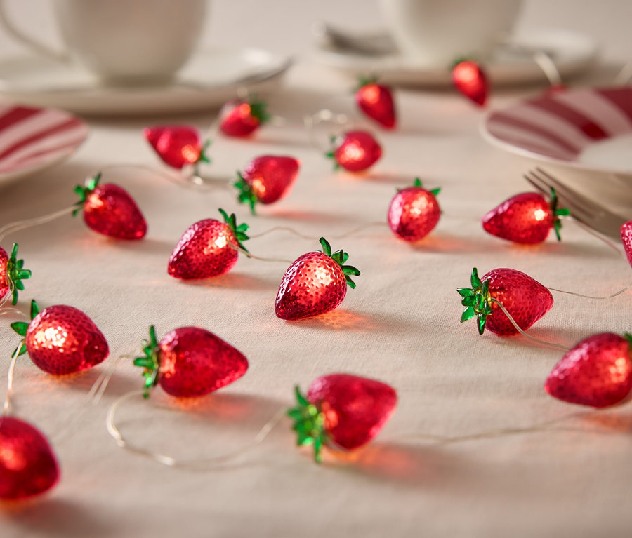 Girlanda świetlna w kształcie truskawek na stole z naczyniami.