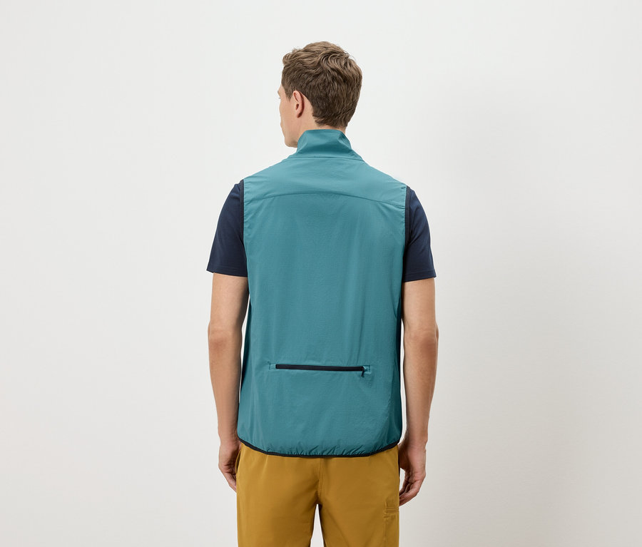 Mężczyzna od tyłu w granatowej koszulce i złotych szortach, ma na sobie petroliową kamizelkę z kieszenią na zamek błyskawiczny.