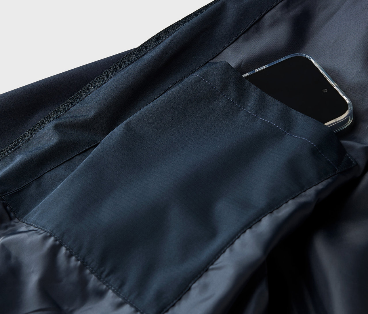 Szczegółowe zdjęcie granatowej kurtki ze smartfonem w kieszeni.