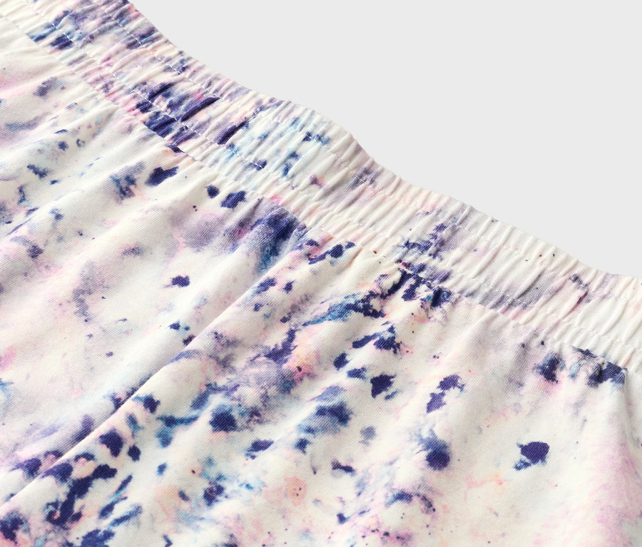 Zbliżenie szortów z elastycznym pasem i wzorem tie-dye w kolorze fioletowym, niebieskim i różowym.