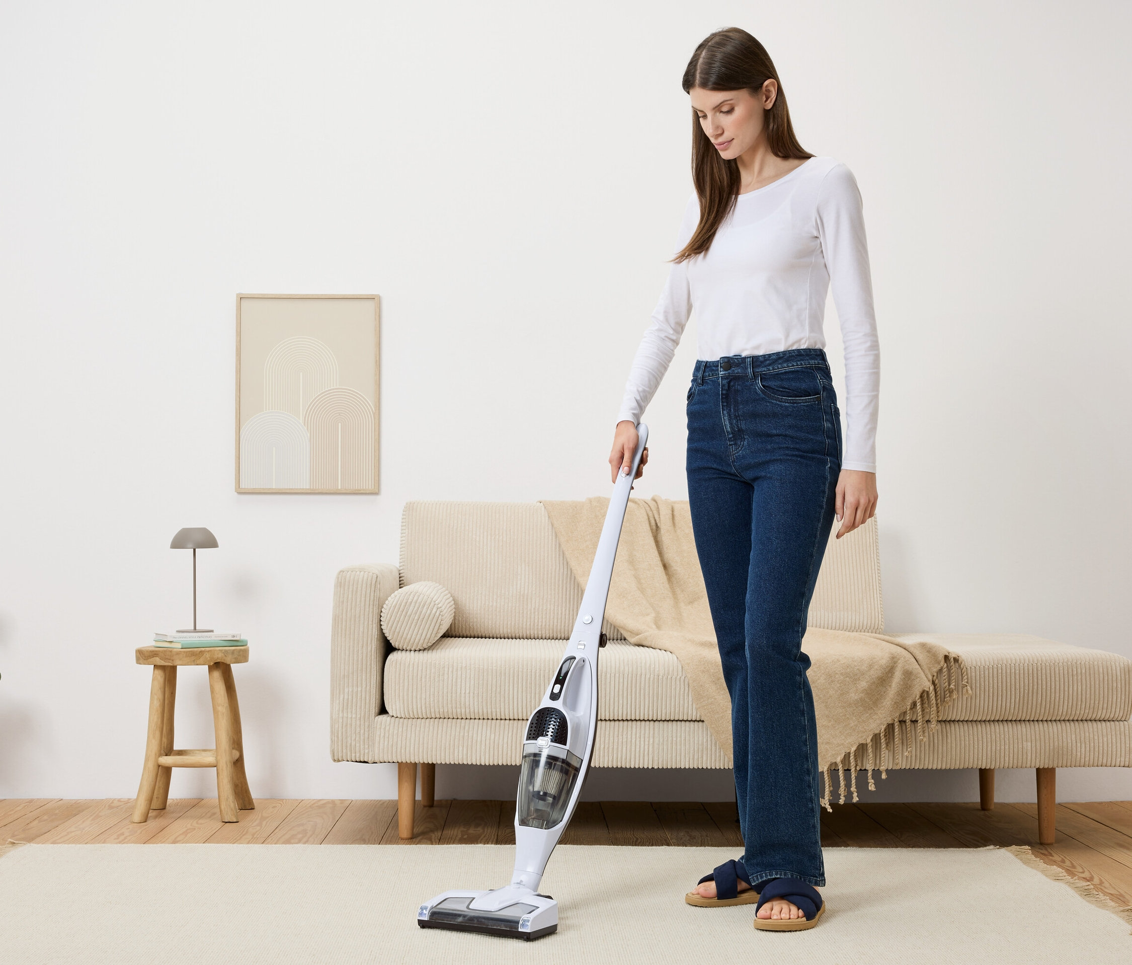 Kobieta odkurza beżowy dywan w salonie białym odkurzaczem akumulatorowym.