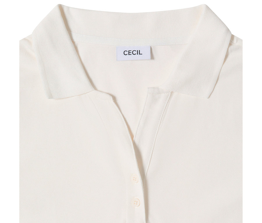 Zbliżenie na białą koszulkę polo CECIL z rękawem 3/4, przedstawiające kołnierzyk, dekolt w serek z dwoma jasnymi guzikami i metkę z napisem 'CECIL'.