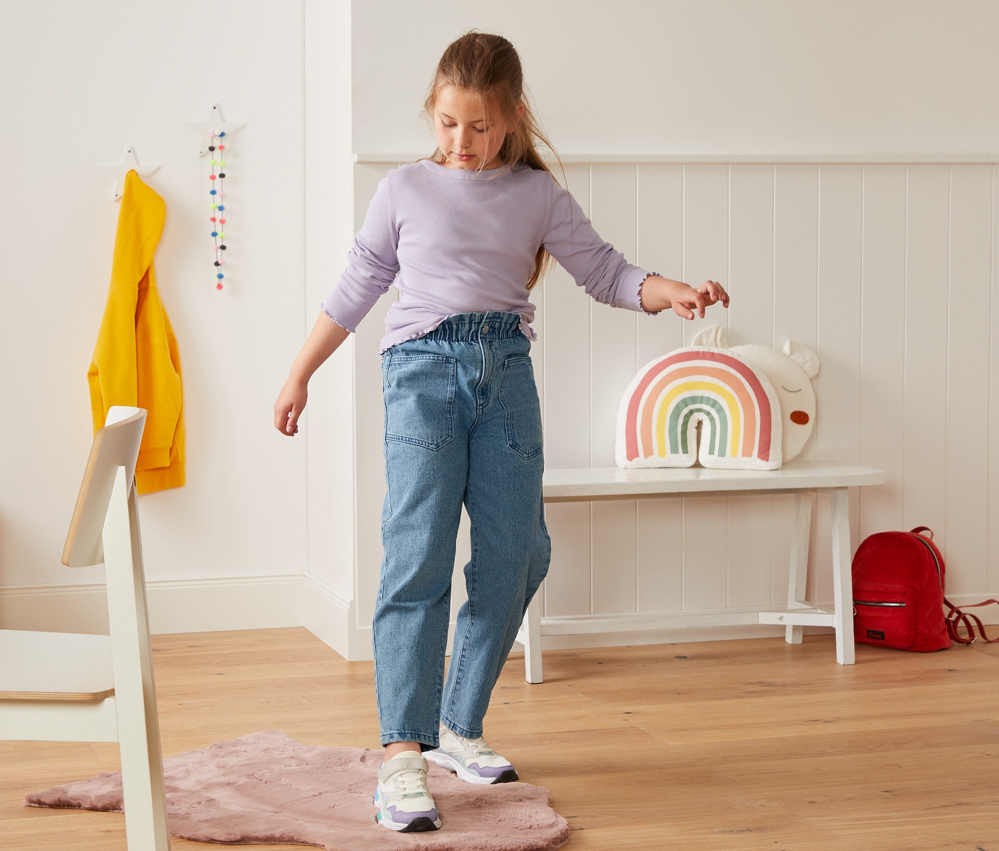 Dziewczyna stoi na różowym dywanie i ma na sobie dżinsy z wysokim stanem.