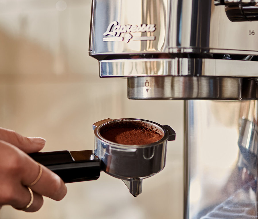 Kobieta wkłada srebrny ekspres kolbowy do kawy »Lapressa« z kawą do ekspresu.