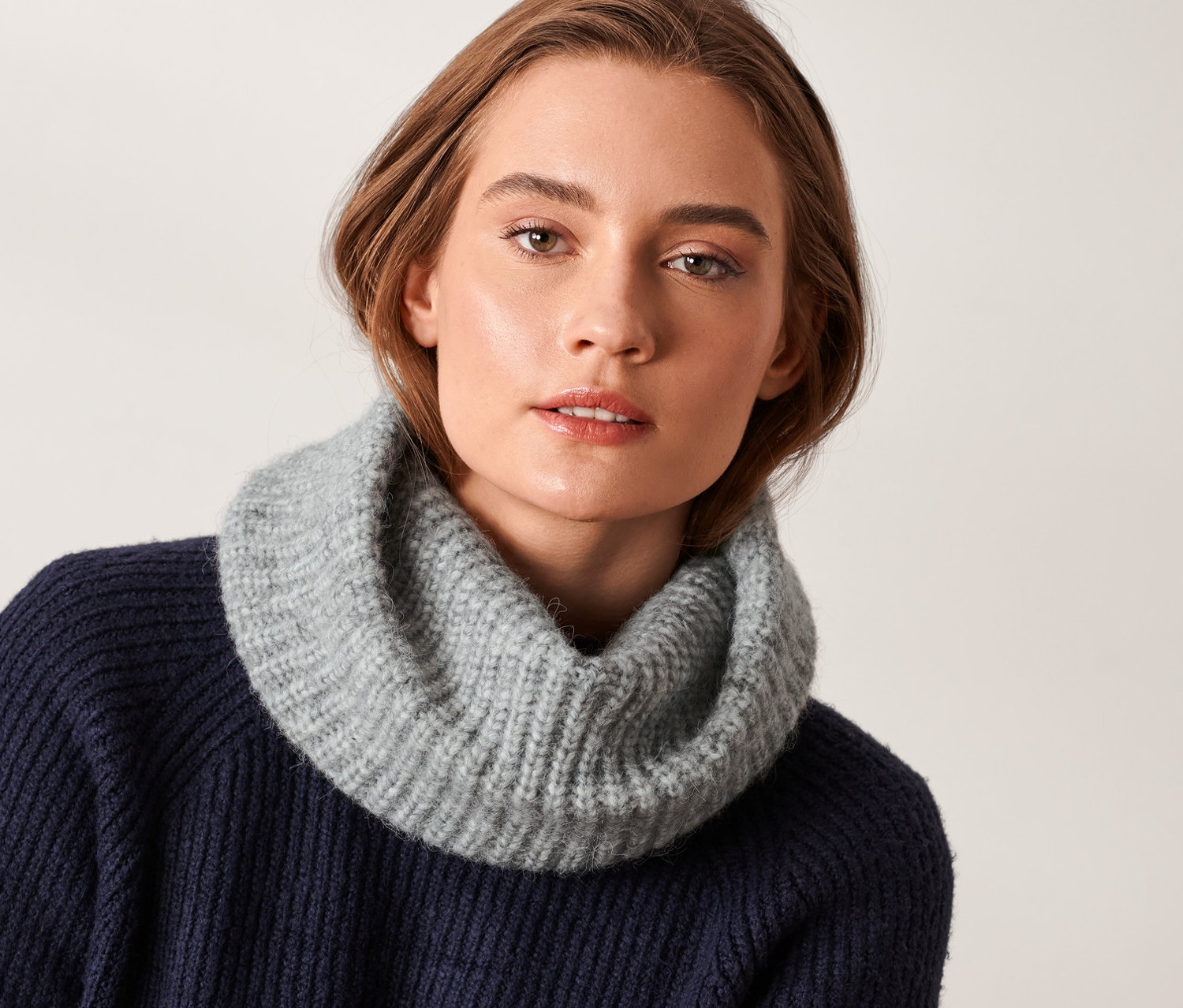 Kobieta ma na sobie szary szal-komin z dzianiny.
