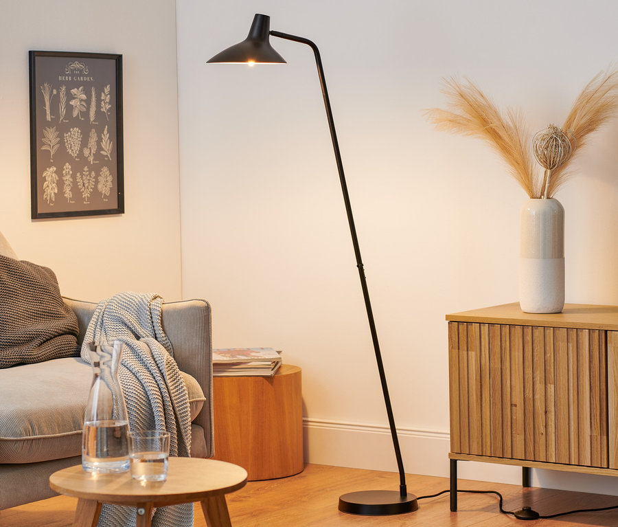 Czarna lampa stojąca Nordlux »Darci« stoi w salonie obok sofy.