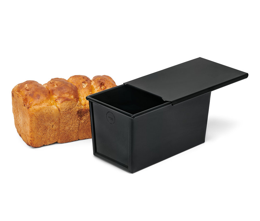 Chleb leży obok czarnej formy do pieczenia chleba.