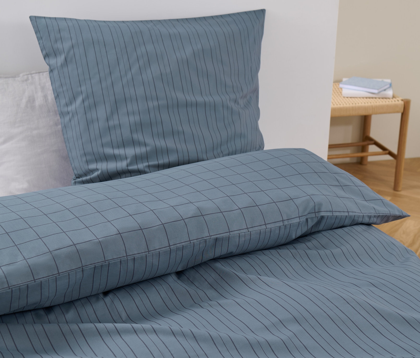 Niebieska pościel z bawełny renforcé o standardowym rozmiarze w paski i kratę leży na łóżku.