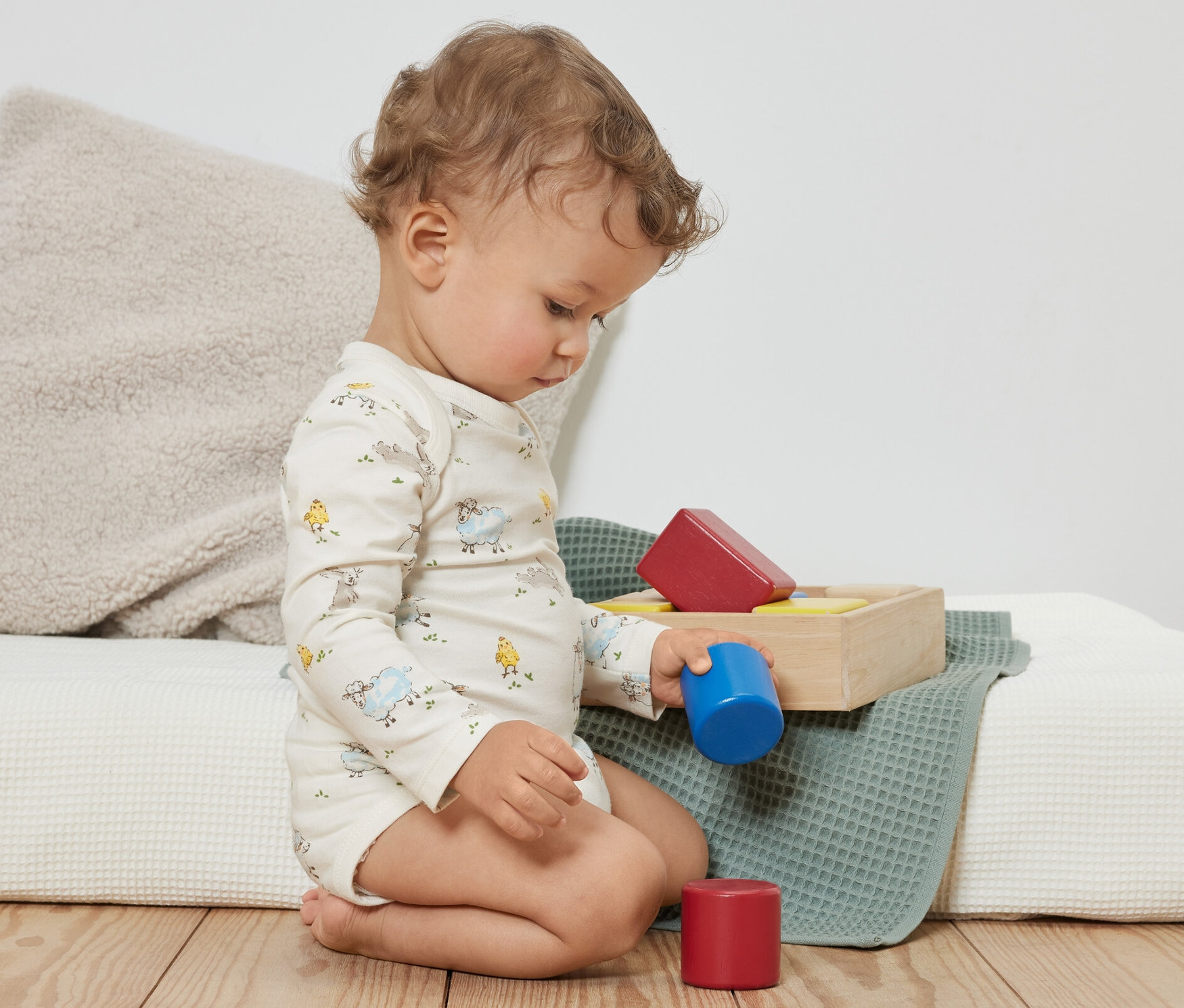 Kędzierzawe dziecko siedzi na podłodze i bawi się kolorowymi klockami. Ubrane jest w niebieskie body niemowlęce rosnące z dzieckiem, 3 pary.