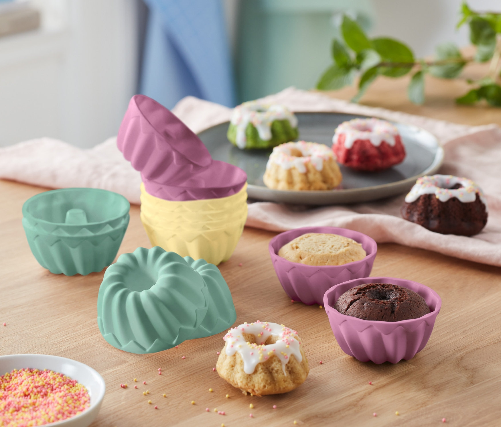 Na drewnianym stole leżą foremki do mini babeczek (12 sztuk) oraz upieczone babeczki.