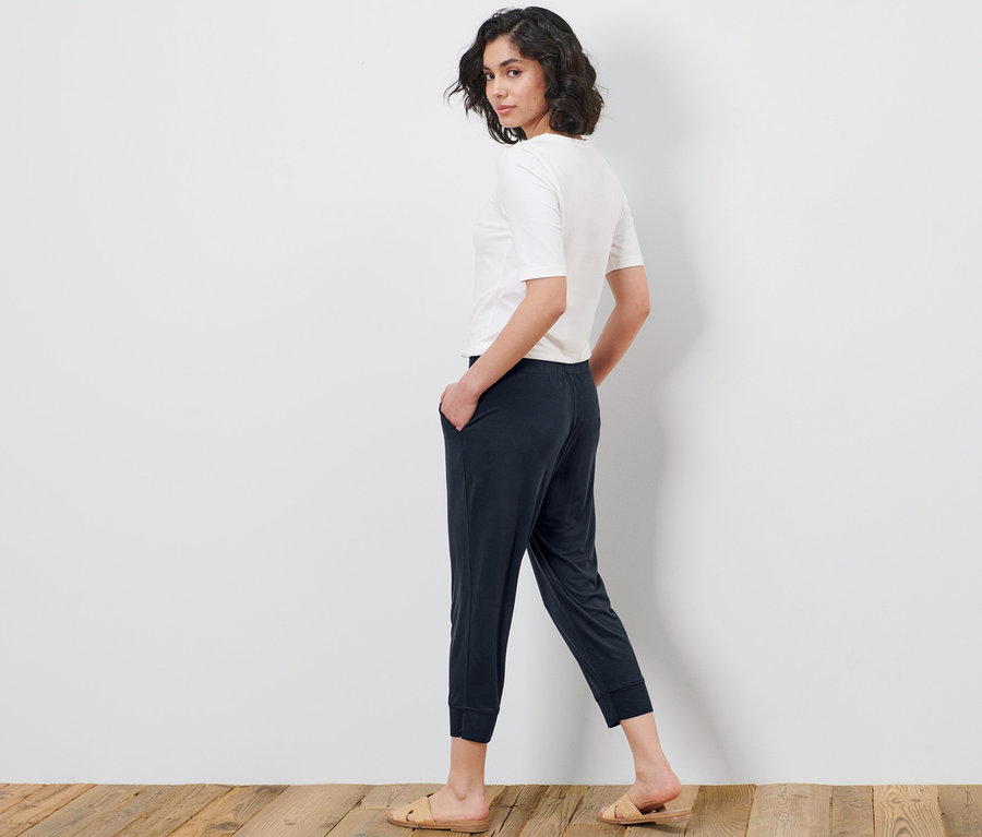 Kobieta patrzy przez ramię i pozuje w spodniach dżersejowych o długości 3/4 i t-shircie.