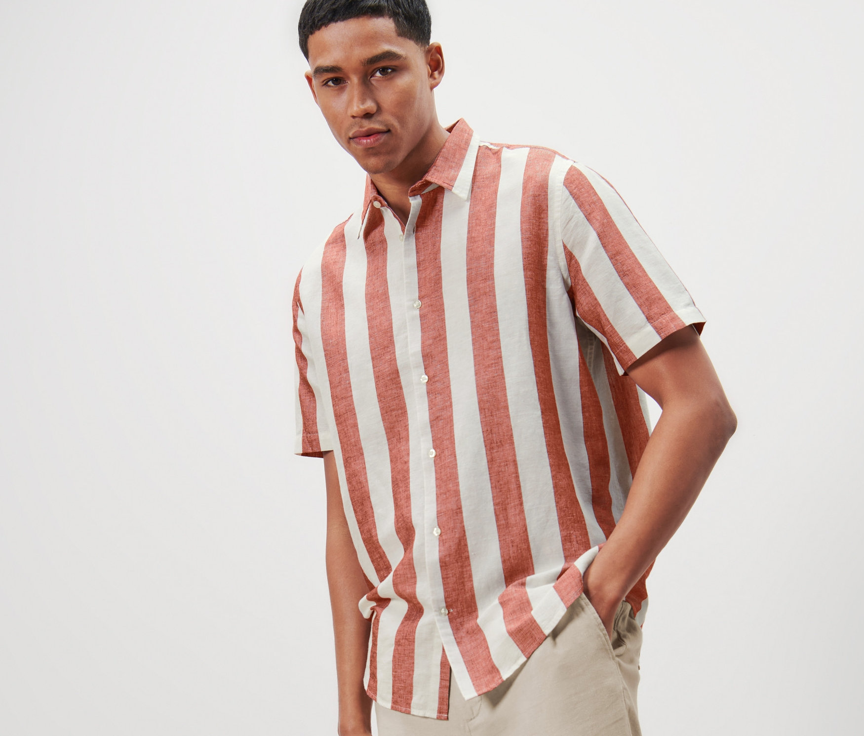 Mężczyzna pozuje w koszuli w paski z krótkim rękawem z zawartością lnu i jasnych spodniach.