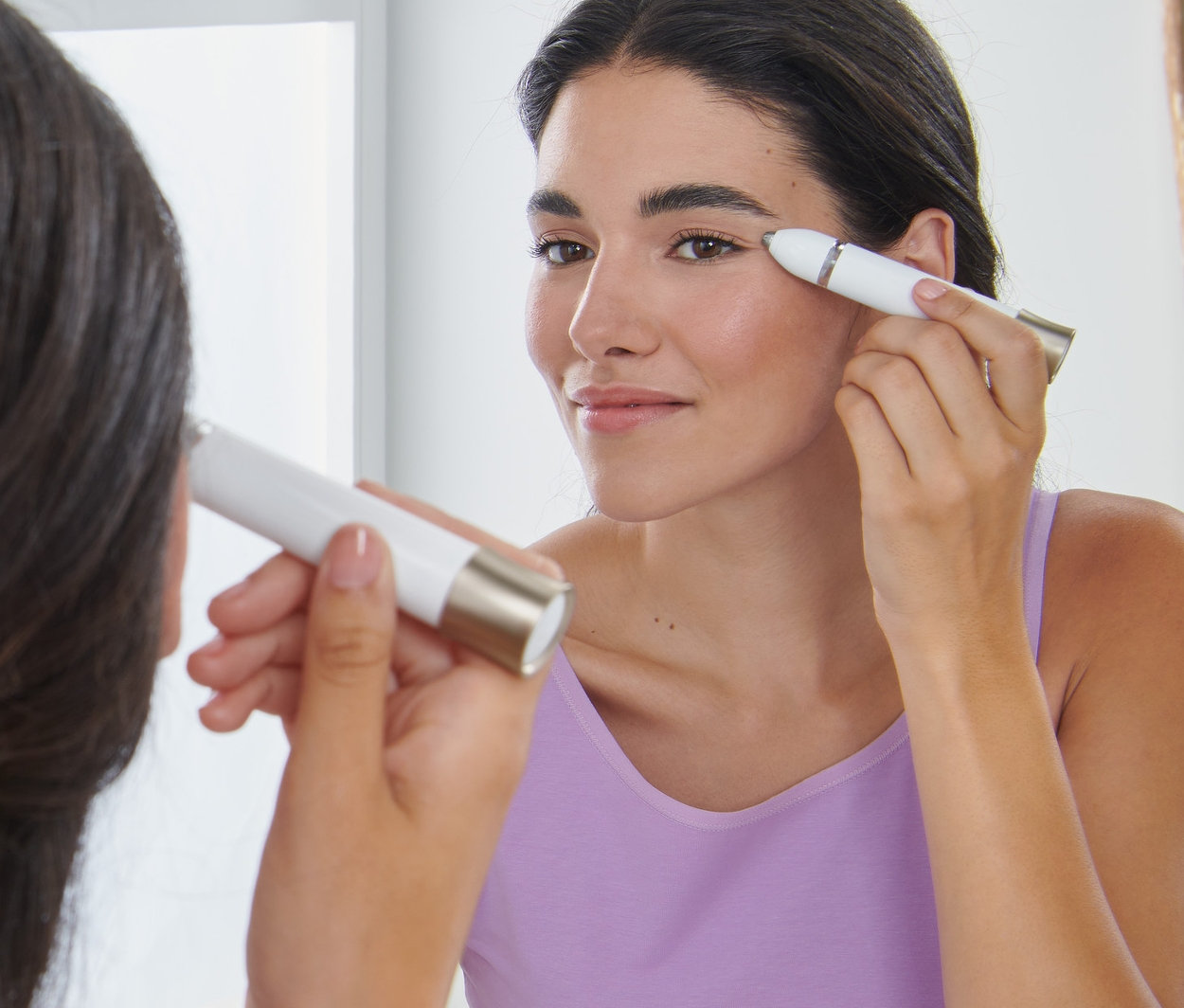 Kobieta stylizuje brwi elektrycznym trymerem do brwi przed lustrem.