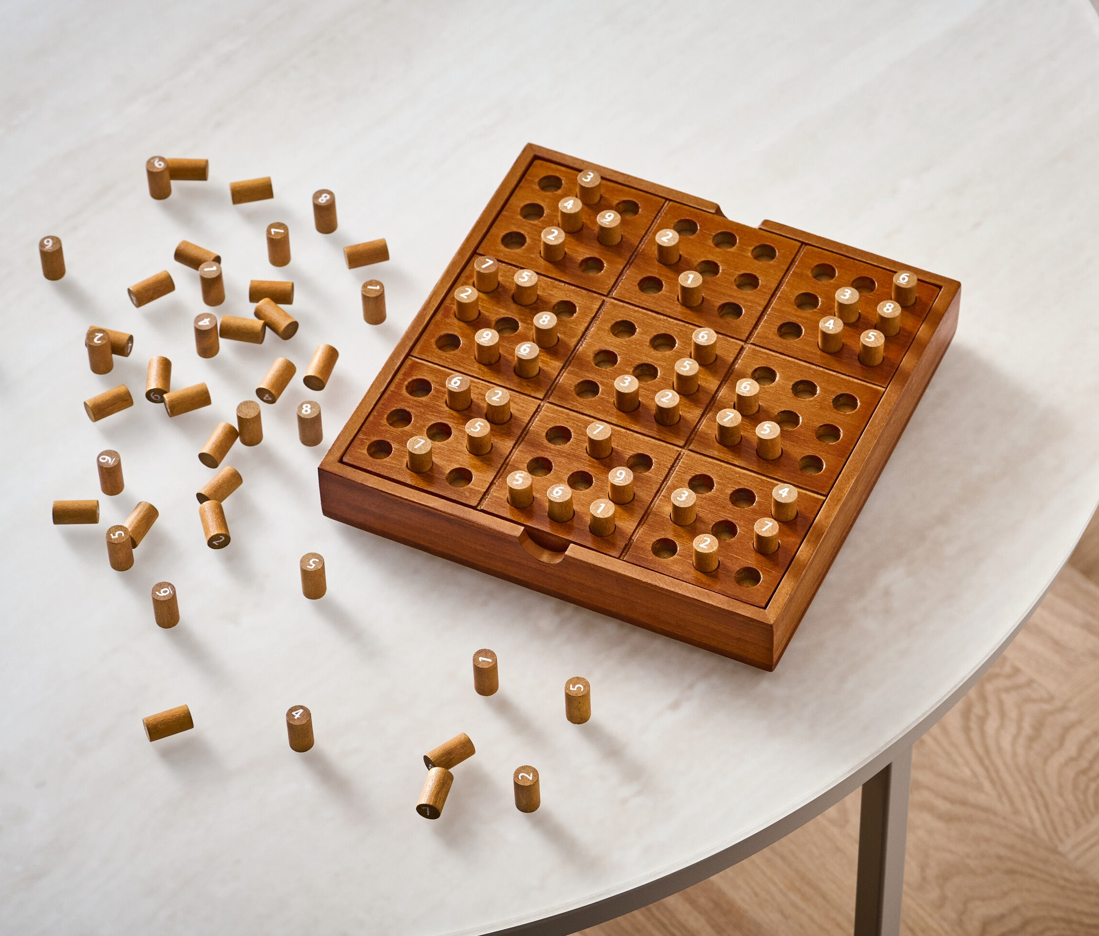 Drewniana gra planszowa „sudoku” z kołkami na białym stole.