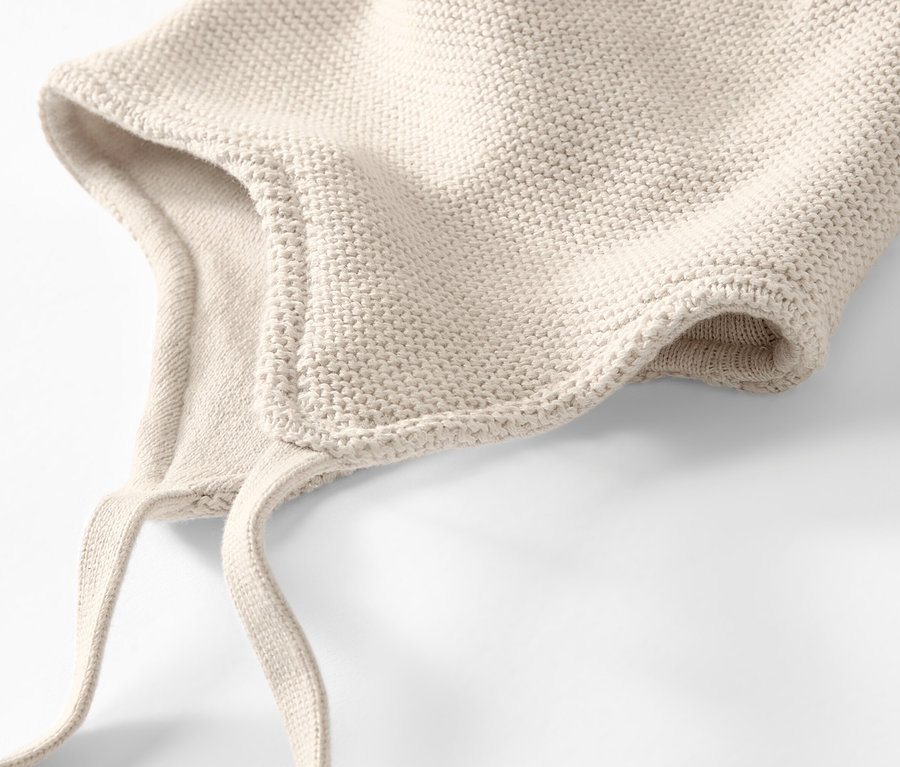 Zbliżenie kremowej czapki i szalika z dzianiny dla niemowląt na białym tle.