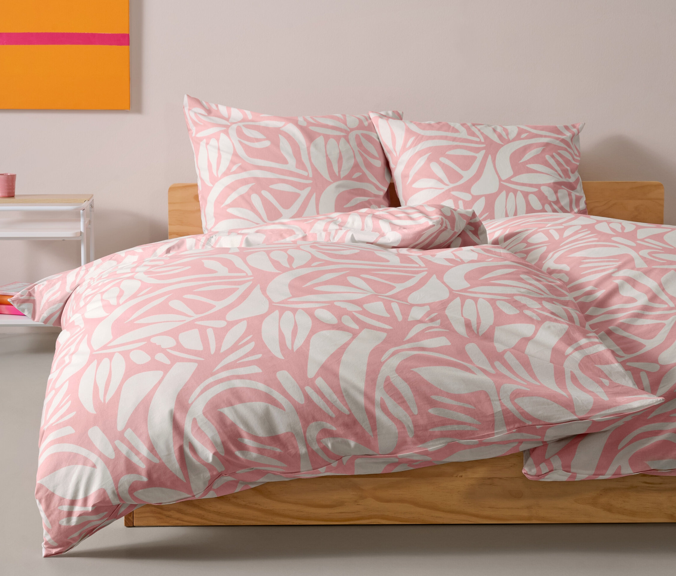 Różowa pościel z bawełny renforcé w standardowym rozmiarze leży na łóżku. Za kołdrą leżą dwie poduszki.