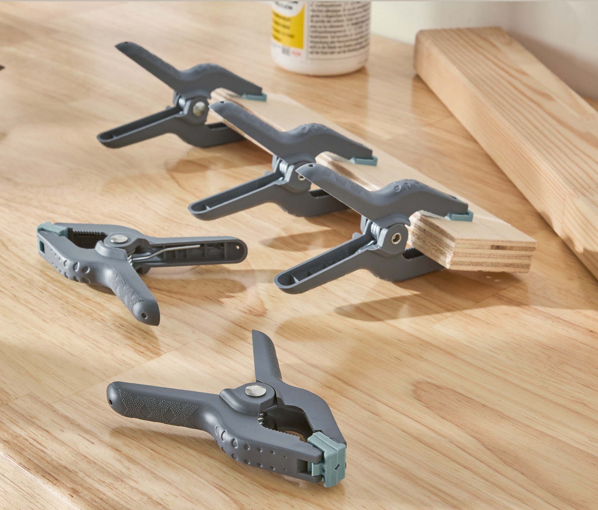Na drewnianej powierzchni leżą wiertarka i pięć szarych zacisków sprężynowych.