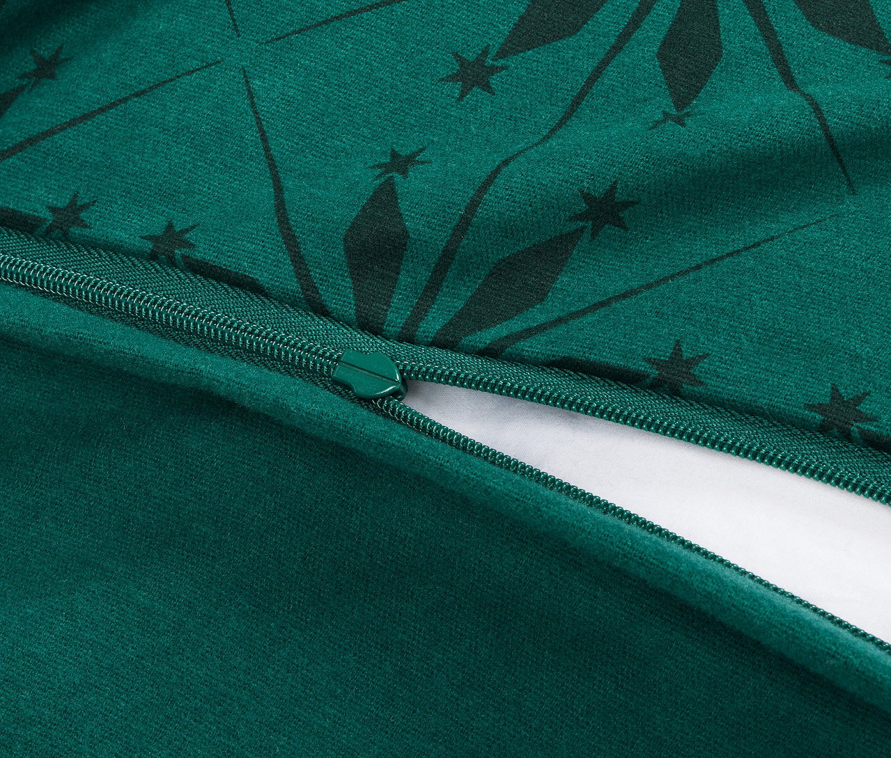 Szczegółowe ujęcie rozpiętego zamka błyskawicznego na zielonej poszewce na kołdrę z ciemnozielonym geometrycznym wzorem.