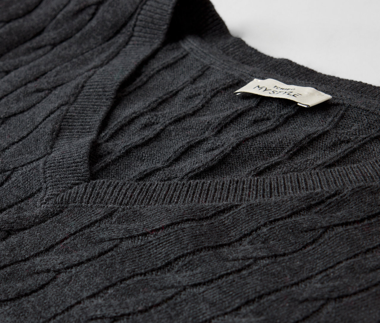 Szczegół szarego swetra w warkocze z dekoltem w serek.