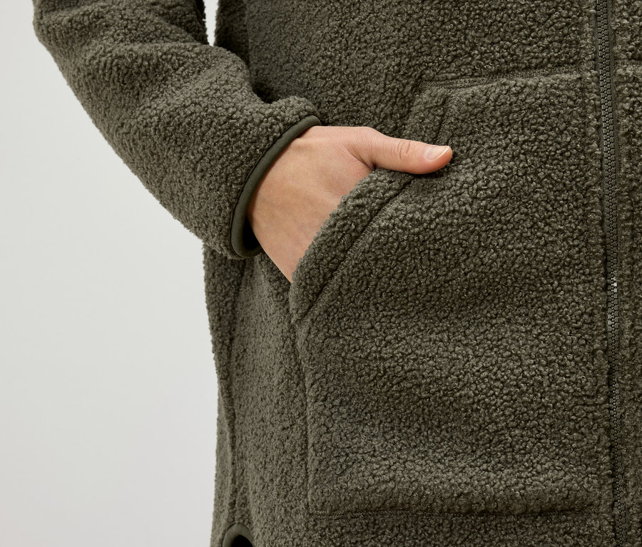 Ręka w kieszeni oliwkowozielonej kurtki z polaru typu baranek.