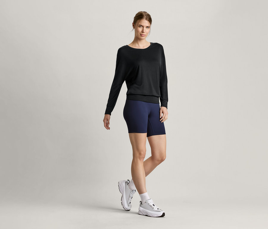 Kobieta nosi czarną koszulkę do sportu i jogi oraz krótkie legginsy sportowe.