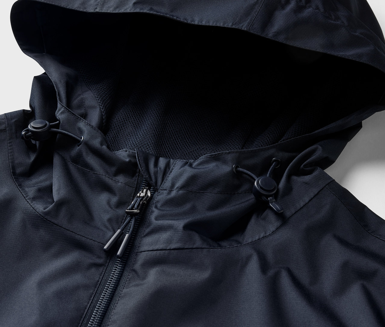 Zbliżenie na granatową kurtkę przeciwdeszczową z kapturem i zamkiem błyskawicznym.