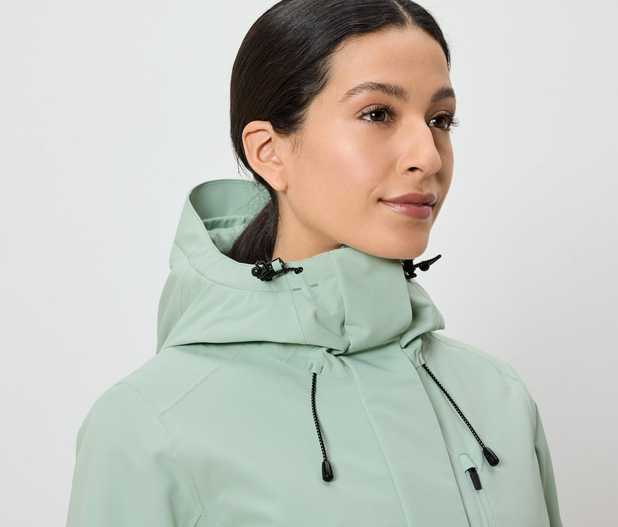 Kobieta ma na sobie jasnozieloną kurtkę z kapturem.